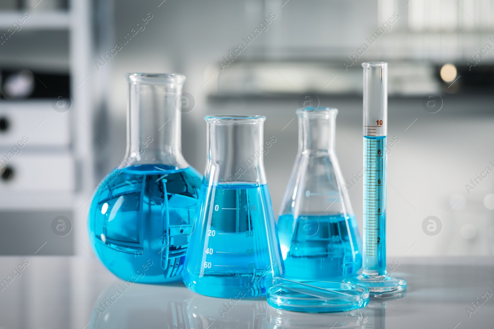 Photo of Different glassware with light blue liquid on table in laboratory