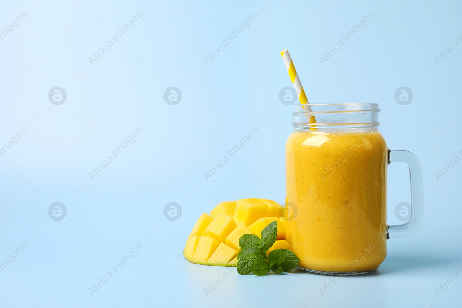 Photo of Mason jar with delicious fruit smoothie and fresh mango on light blue background. Space for text