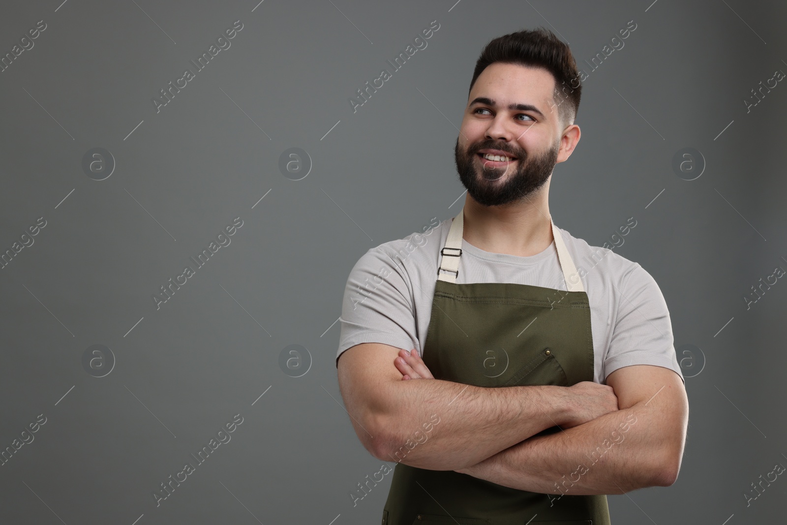 Photo of Smiling man in kitchen apron with crossed arms on grey background. Mockup for design