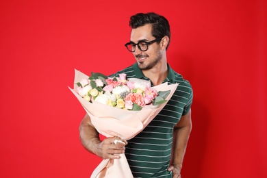 Photo of Young handsome man with beautiful flower bouquet on red background