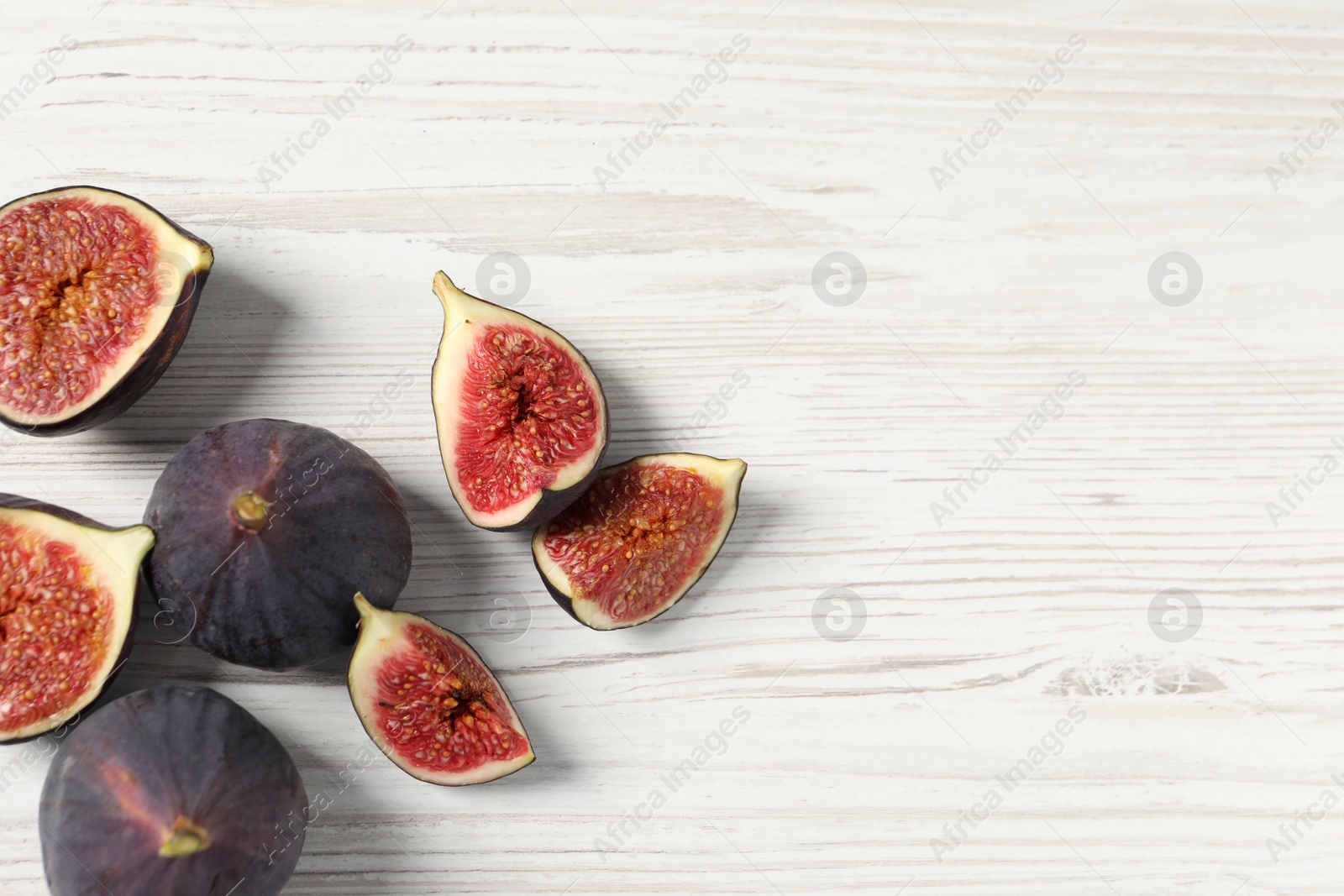 Photo of Whole and cut ripe figs on white wooden table, flat lay. Space for text