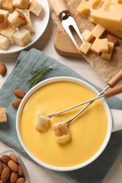 Pot of tasty cheese fondue, bread and almonds on white wooden table, flat lay