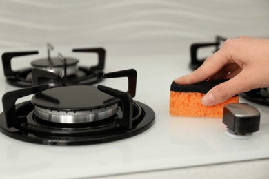 Photo of Woman cleaning gas stove with sponge, closeup