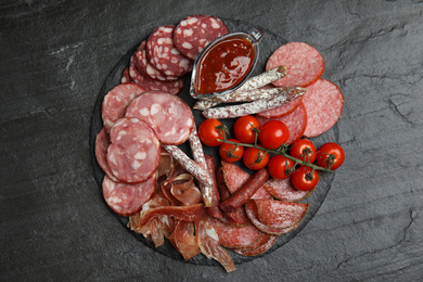 Photo of Different types of sausages with tomatoes served on black table, flat lay