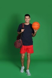 Photo of Handsome man with sports bag and basketball ball on green background