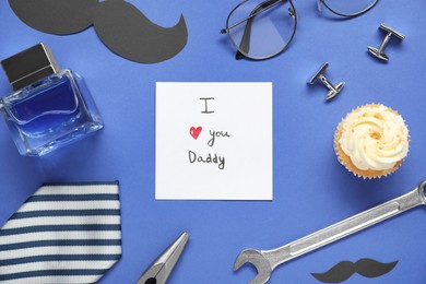 Photo of Father's day celebration. Card with phrase I Love You Daddy, delicious cupcake and men accessories on blue background, flat lay
