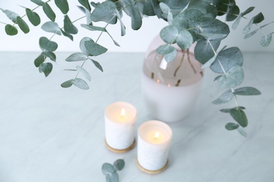 Photo of Beautiful eucalyptus branches and burning candles on grey table, closeup. Interior element