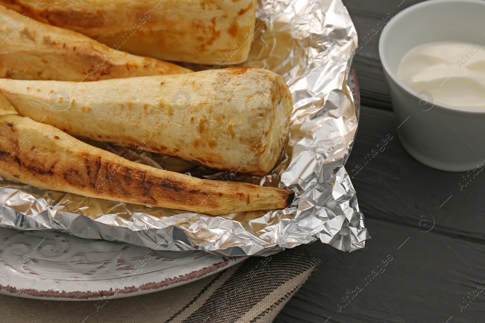 Photo of Tasty baked parsnips and sauce on black wooden table, closeup