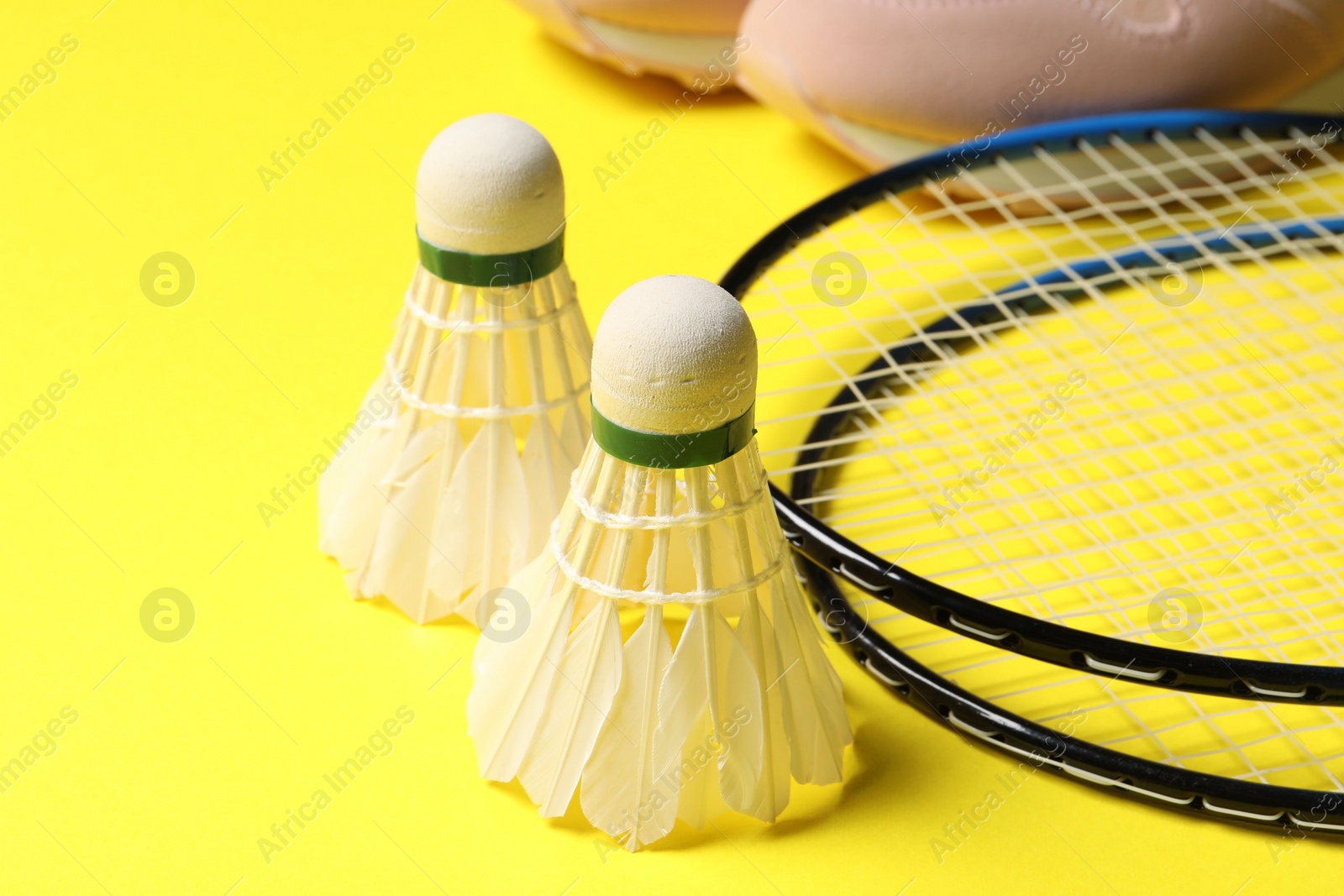 Photo of Feather badminton shuttlecocks, rackets and sneakers on yellow background, closeup