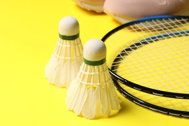 Photo of Feather badminton shuttlecocks, rackets and sneakers on yellow background, closeup