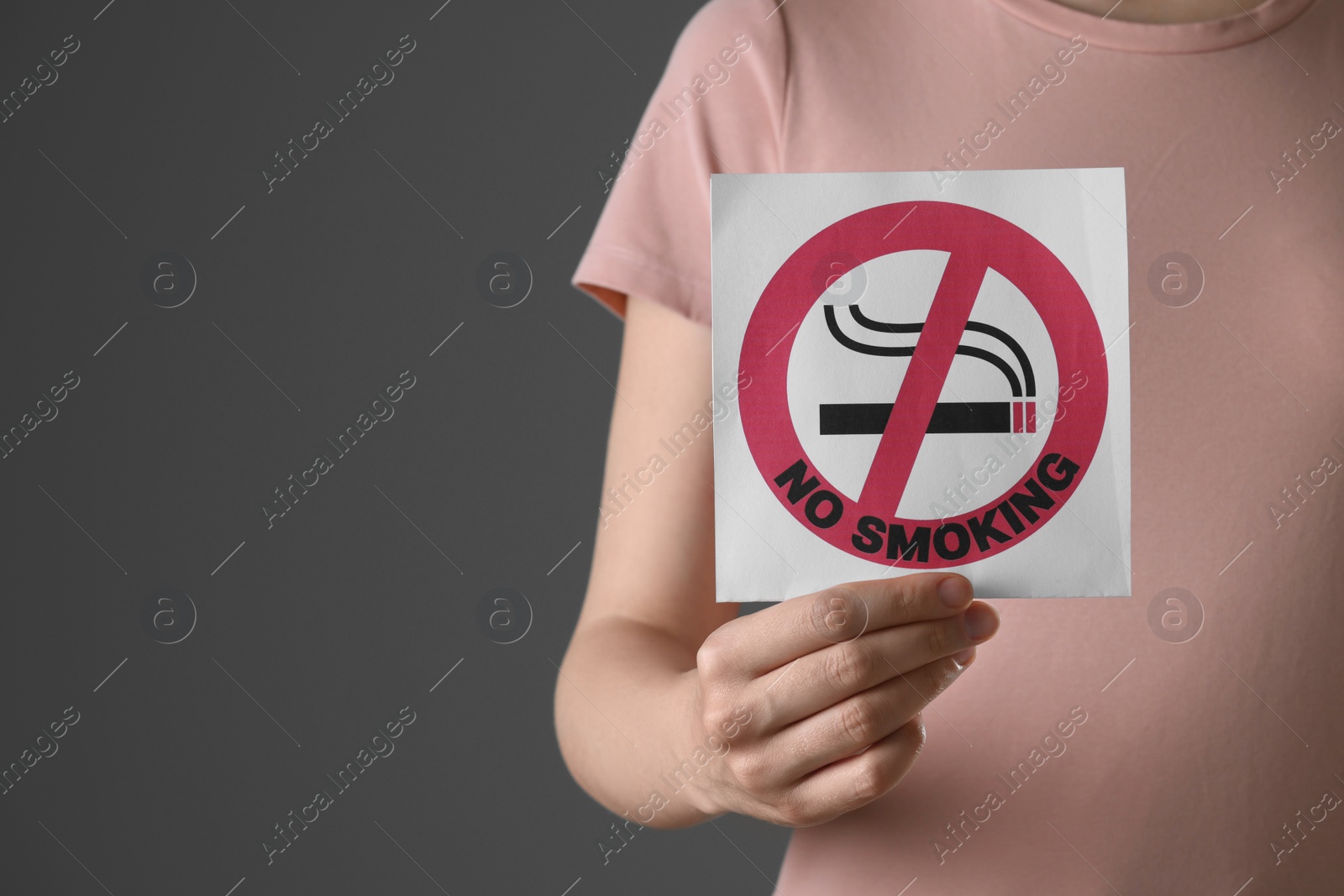 Photo of Woman holding card with no smoking sign on gray background, closeup. Space for text