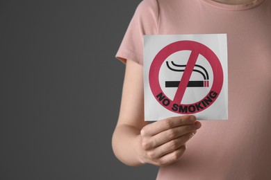 Woman holding card with no smoking sign on gray background, closeup. Space for text