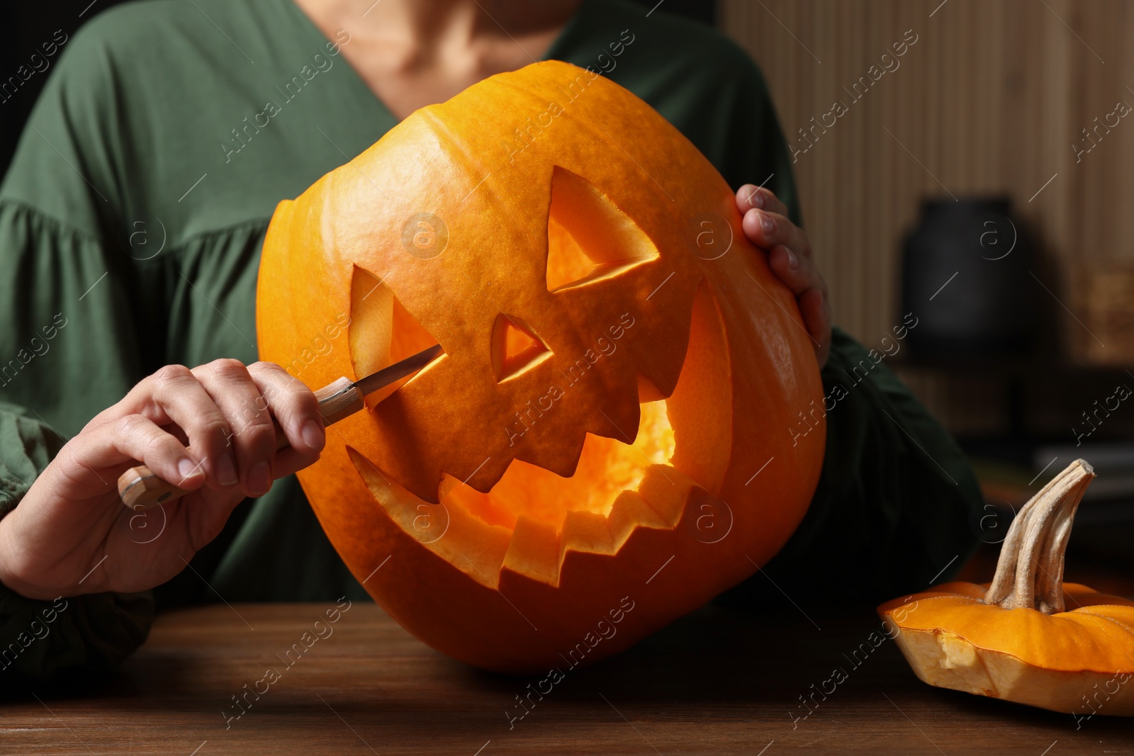 Photo of Woman carving pumpkin for Halloween at wooden table, closeup