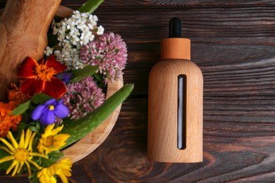 Photo of Glass bottle of aromatic essential oil and mortar with different herbs on wooden table, flat lay