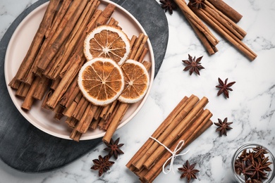 Aromatic cinnamon sticks, dry orange and anise on white marble table, flat lay