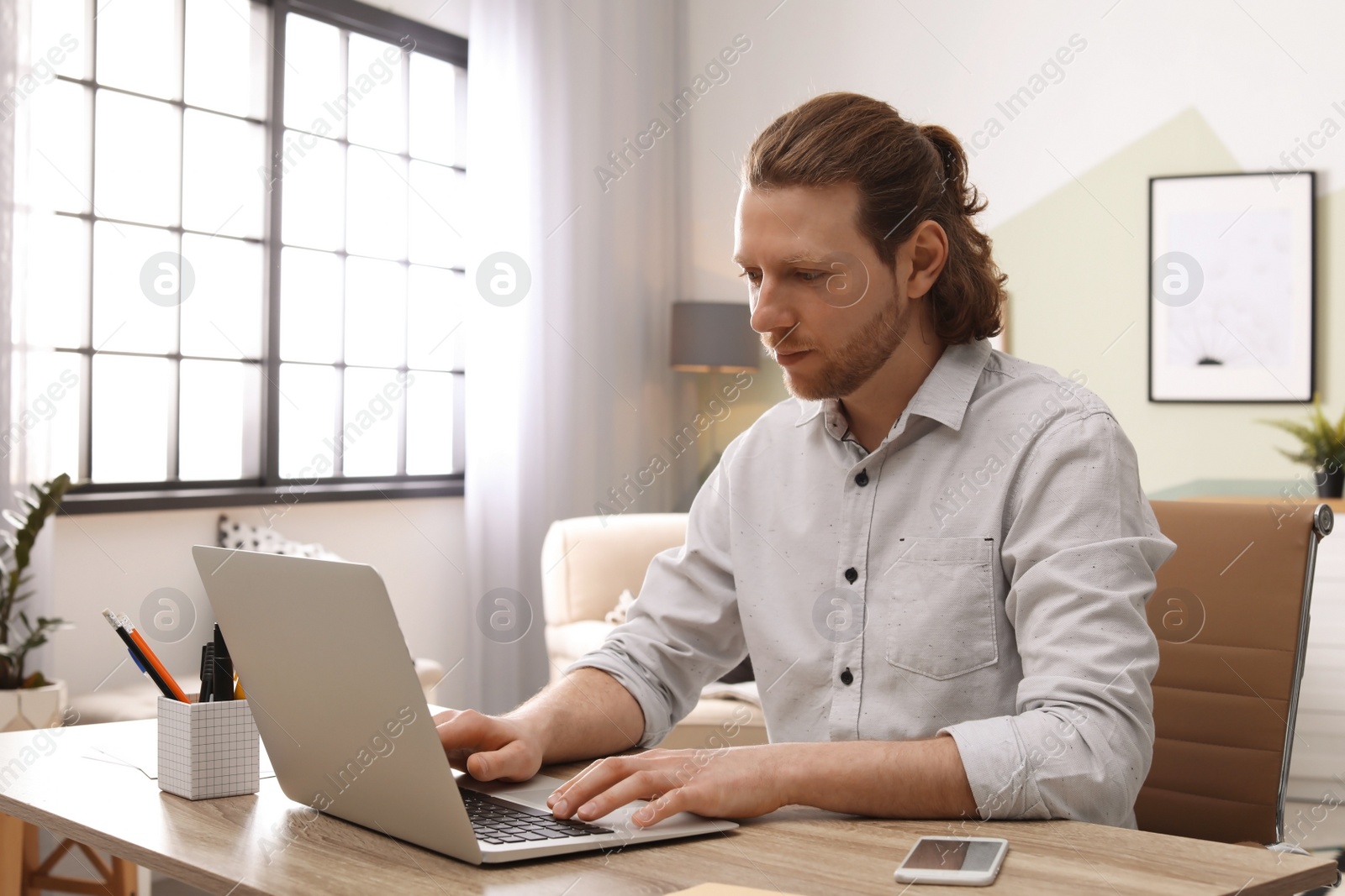 Photo of Young man working with laptop at desk in home office