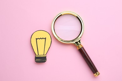 Magnifying glass and paper light bulb on pink background, flat lay