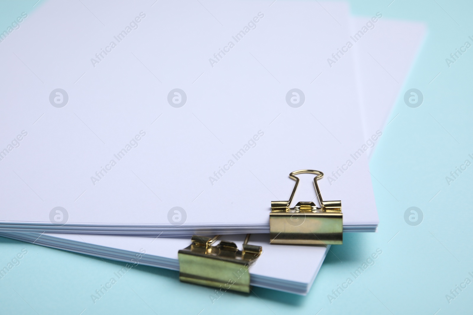 Photo of Sheets of paper with clips on light blue background, closeup