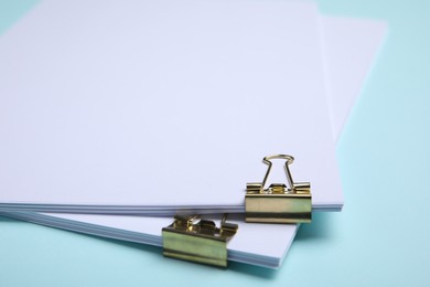 Photo of Sheets of paper with clips on light blue background, closeup