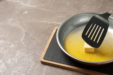 Photo of Frying pan with melting butter and spatula on grey table. Space for text