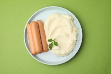 Photo of Delicious boiled sausages, mashed potato and parsley on green background, top view