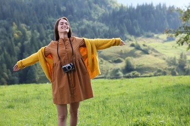 Photo of Happy woman with camera dancing on meadow in mountains