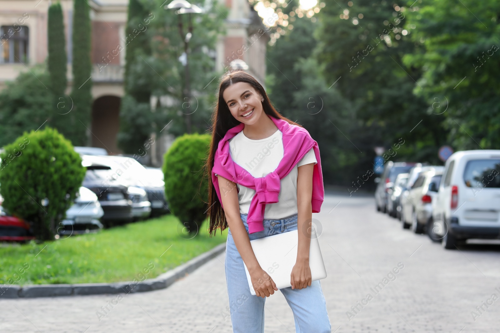 Photo of Happy young woman holding modern laptop on city street