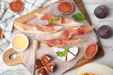 Photo of Tasty melon, jamon and figs served on white wooden table, flat lay