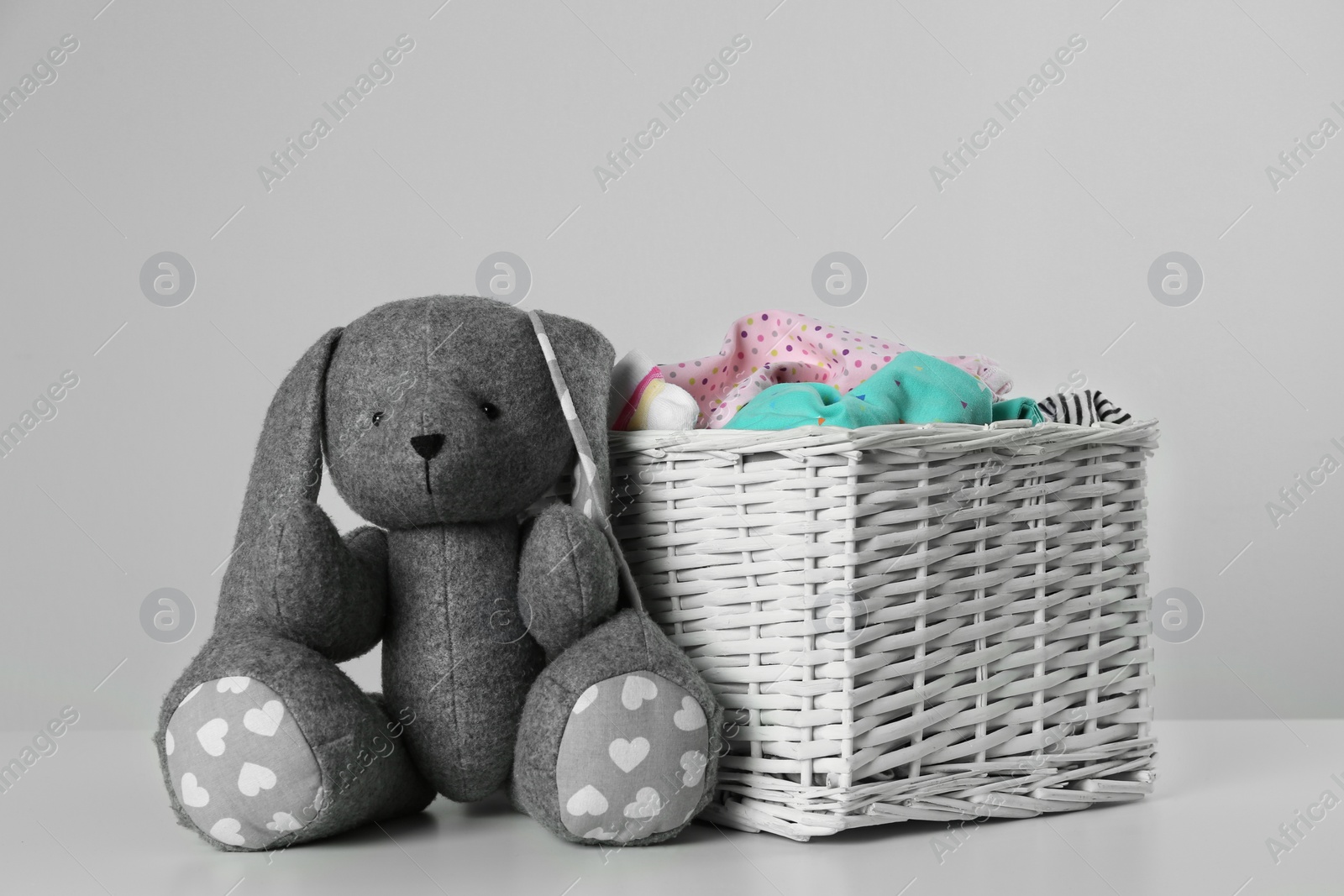 Photo of Wicker laundry basket with different children's clothes and toy on light background