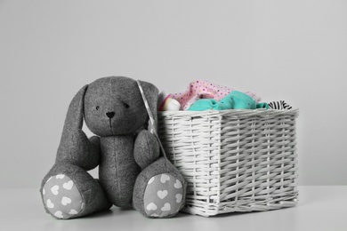 Wicker laundry basket with different children's clothes and toy on light background