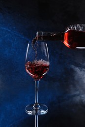 Photo of Pouring pink wine from bottle into glass on color background