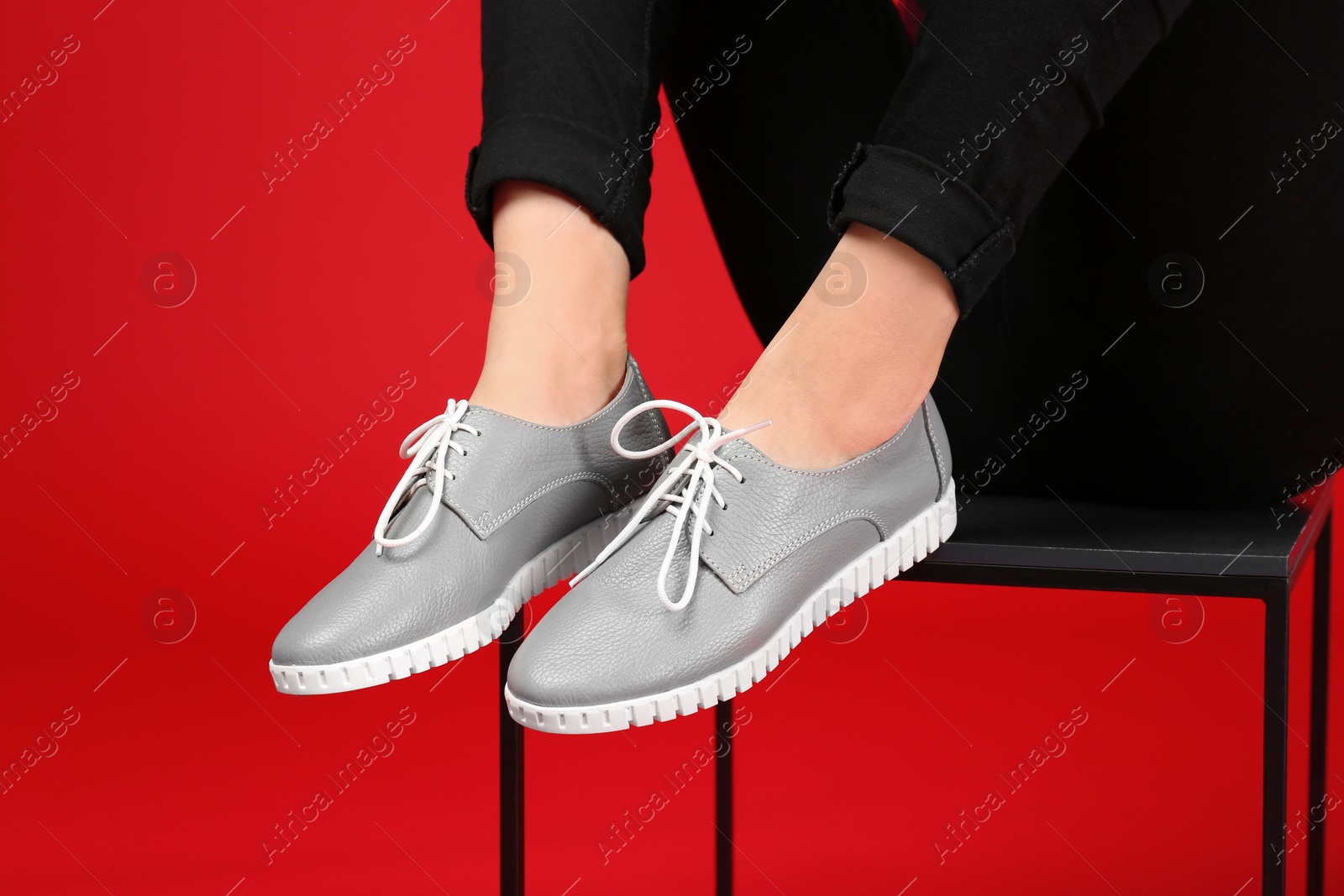 Photo of Woman in stylish shoes sitting on stool against color background