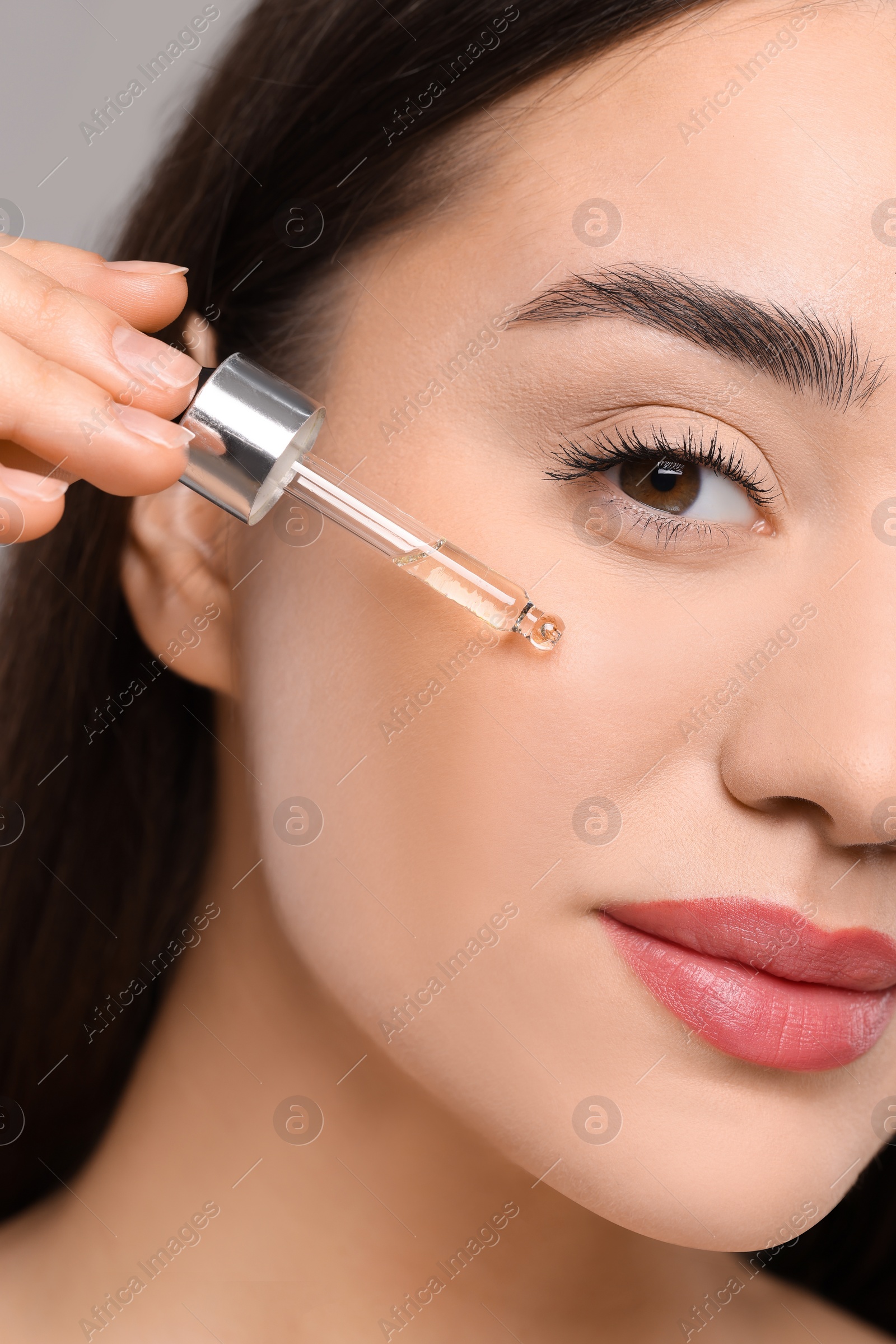 Photo of Young woman applying essential oil onto face, closeup