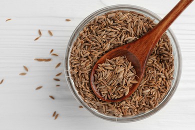 Bowl of caraway seeds and spoon on white wooden table, flat lay