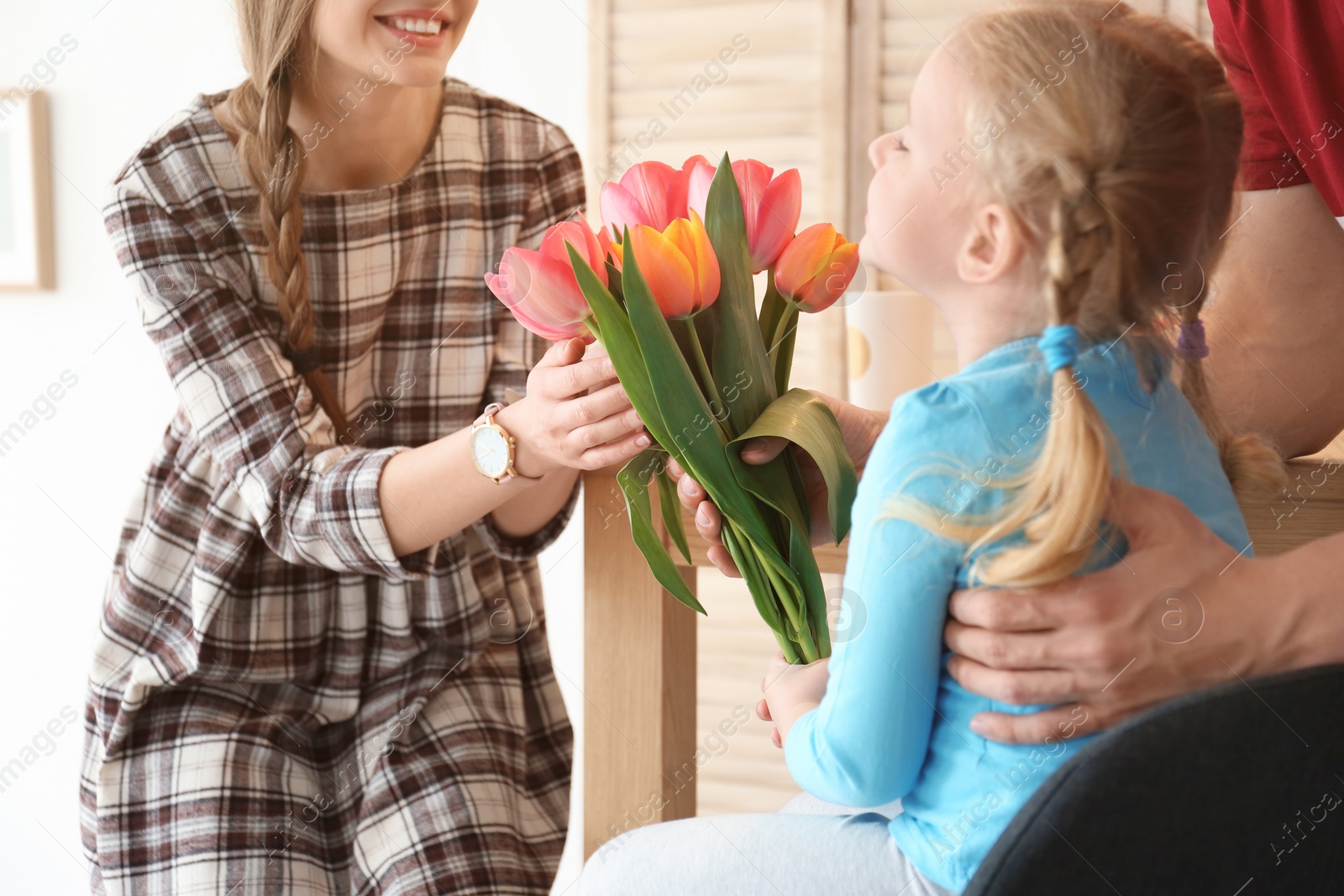 Photo of Happy woman receiving flowers from husband and daughter at home. Mother's day celebration