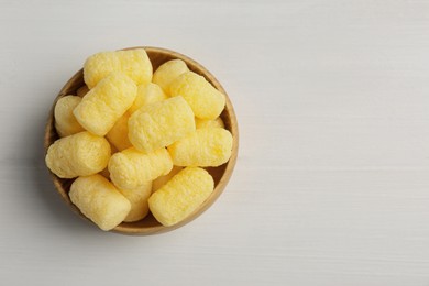 Photo of Bowl of delicious crispy corn sticks on white wooden table, top view. Space for text