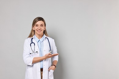 Portrait of happy doctor with stethoscope on light grey background, space for text