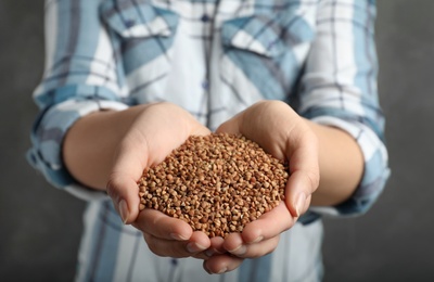 Woman holding raw buckwheat in hands on grey background, closeup