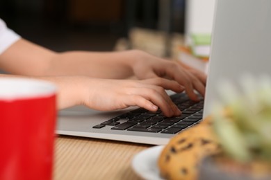 Photo of Little girl using laptop at table indoors, closeup. Internet addiction