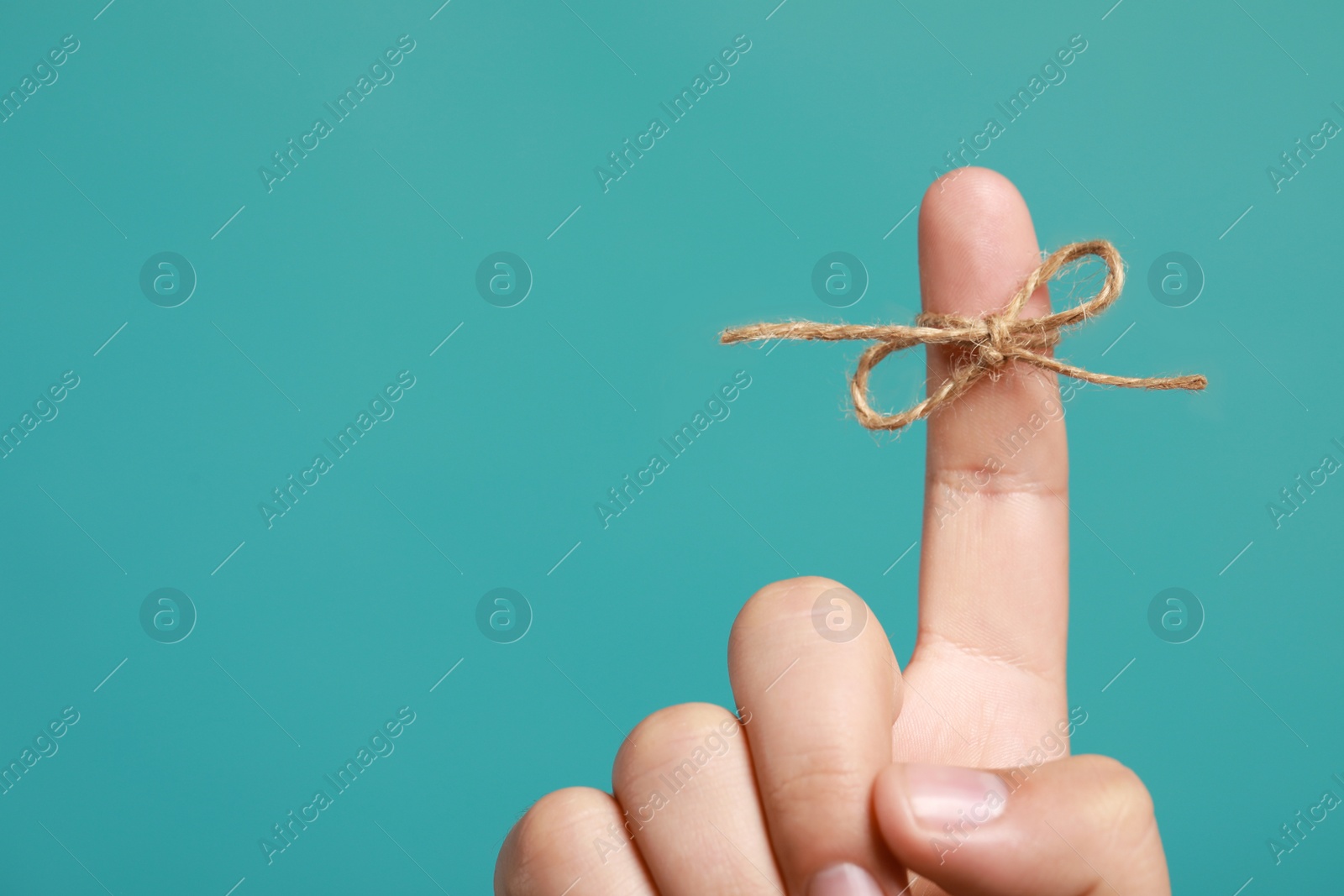 Photo of Man showing index finger with tied bow as reminder on turquoise background, closeup. Space for text