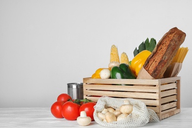 Crate with fresh vegetables and other products on wooden table against light background, space for text