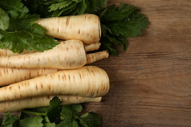 Photo of Fresh ripe parsnips with leaves on wooden table, flat lay. Space for text