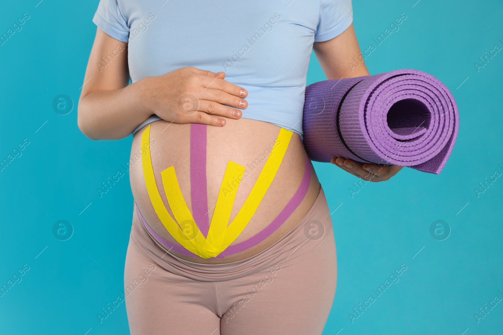 Photo of Pregnant woman with kinesio tapes holding sport mat on light blue background, closeup