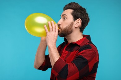 Photo of Man inflating yellow balloon on light blue background