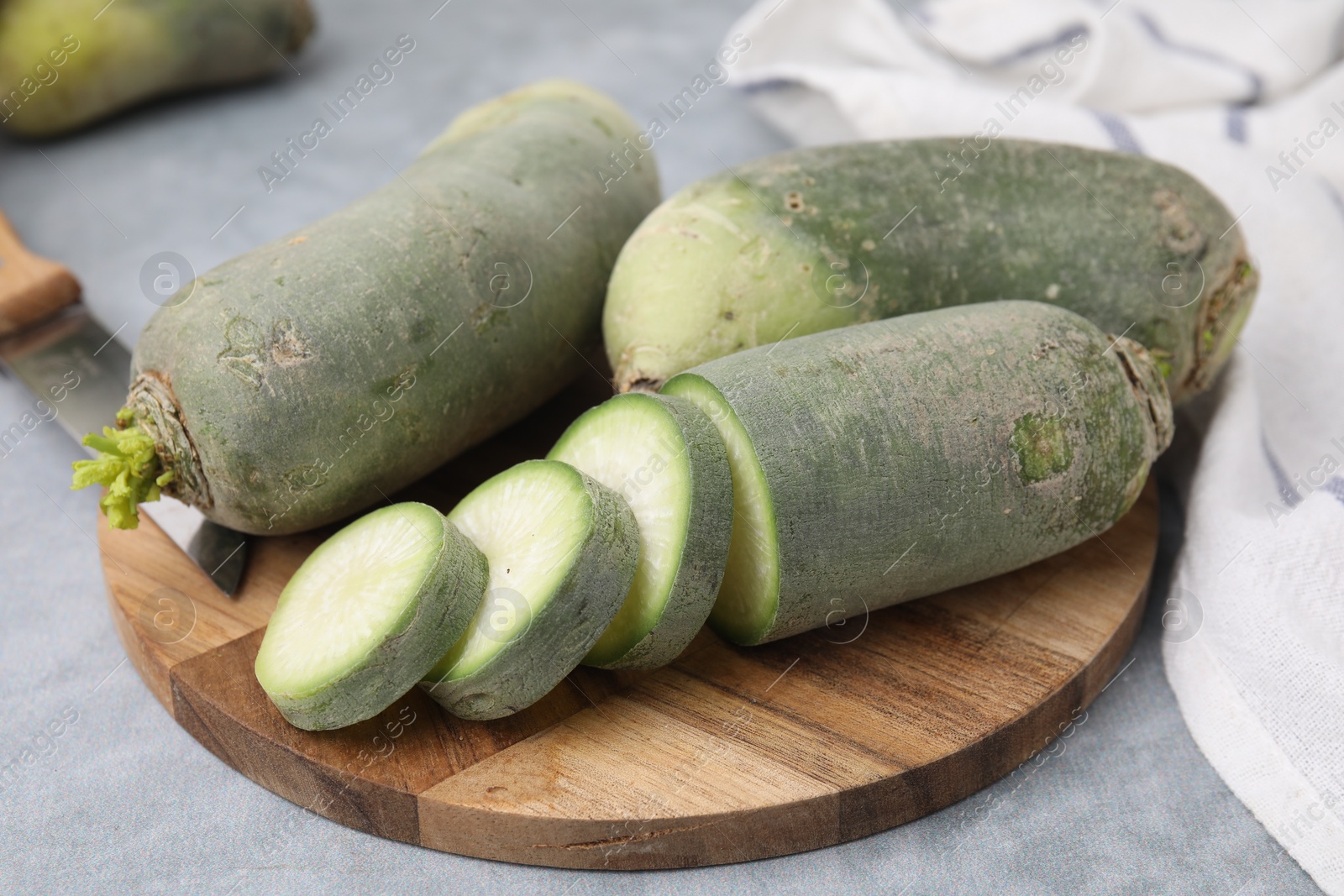 Photo of Green daikon radishes and knife on light grey table