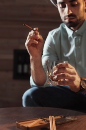 Man with glass of whiskey and cigar sitting at table indoors