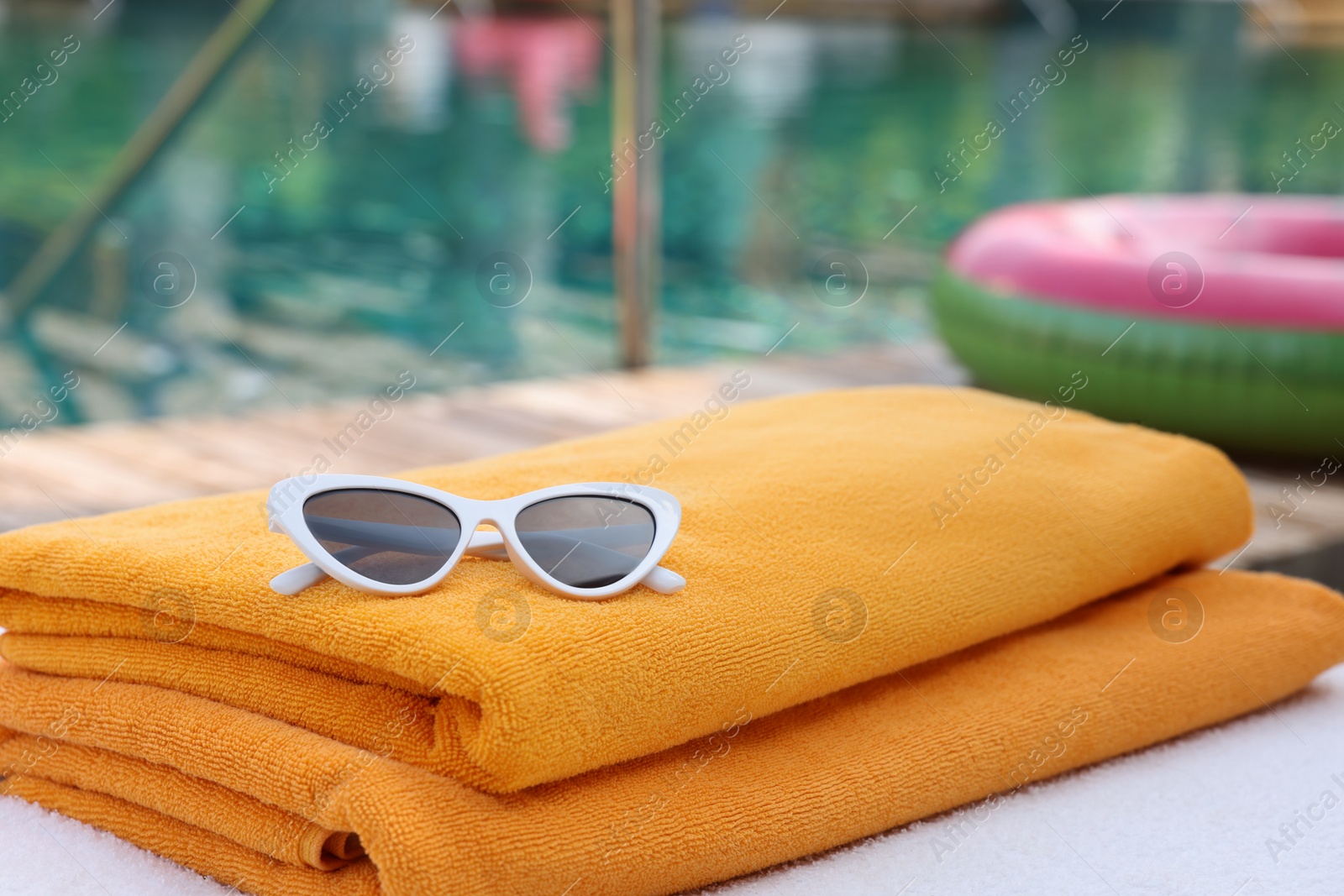 Photo of Beach towels and sunglasses on sun lounger near outdoor swimming pool, closeup. Luxury resort