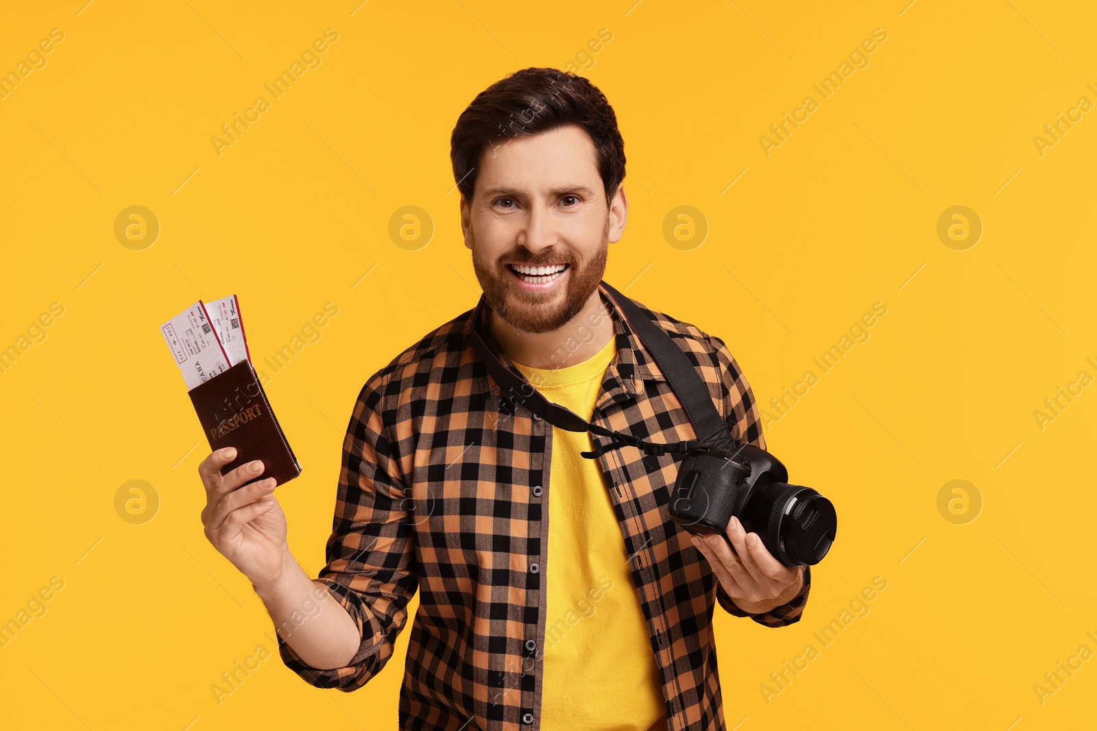 Photo of Smiling man with passport, tickets and camera on yellow background