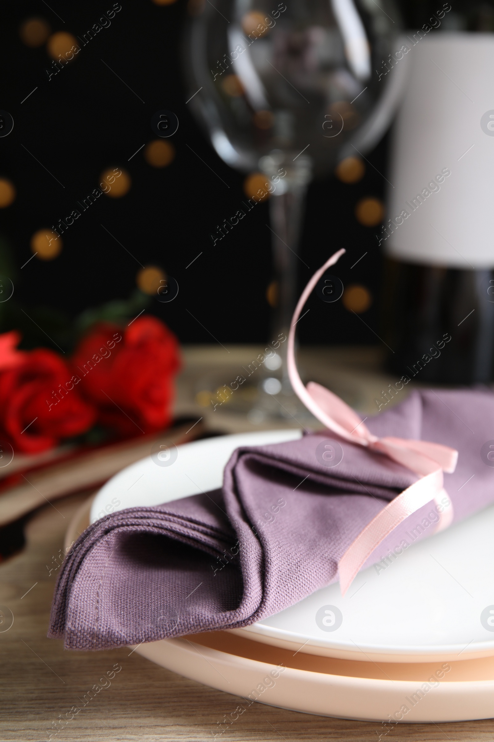 Photo of Beautiful place setting for romantic dinner on table against black background with blurred lights, closeup. Valentine's day celebration