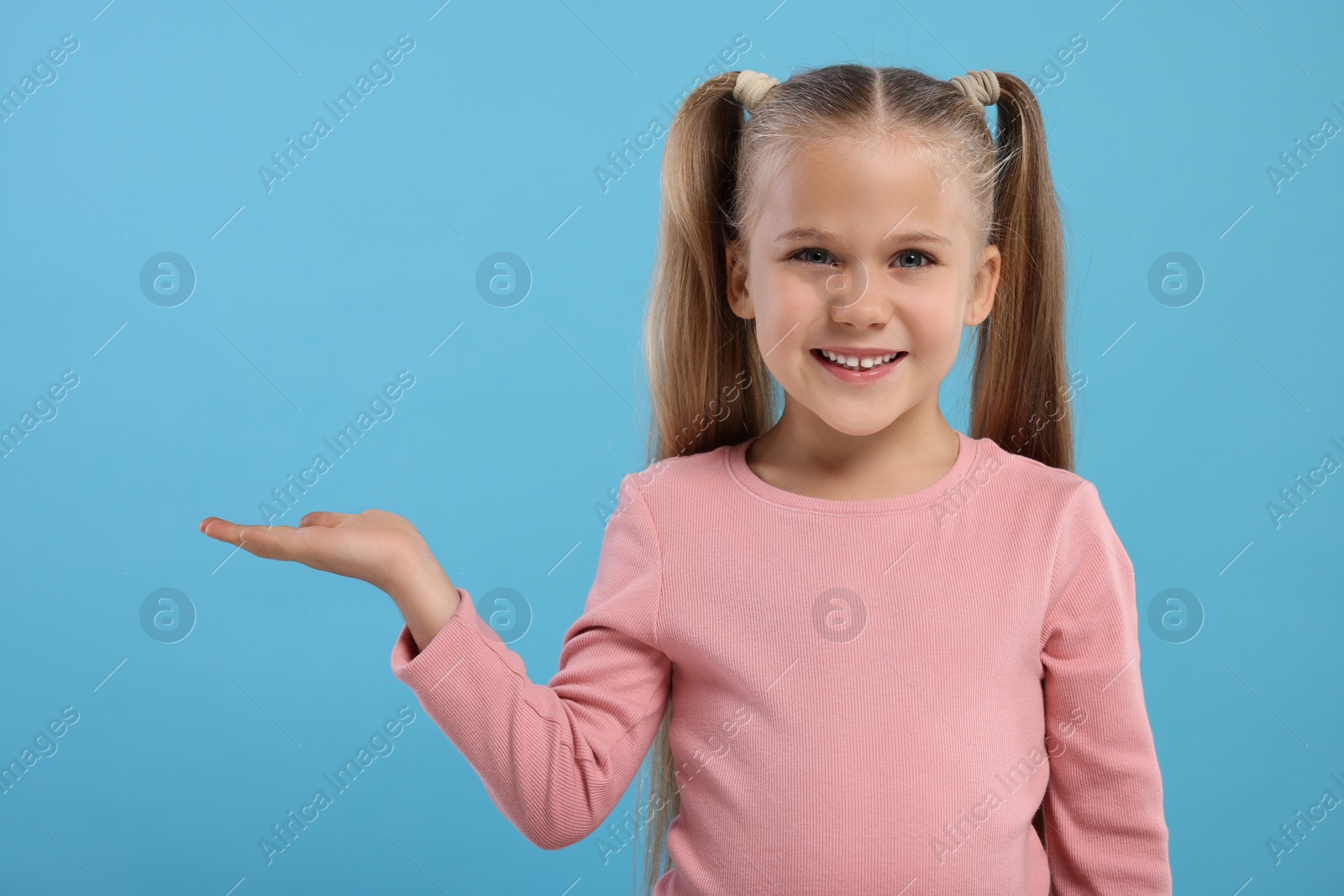 Photo of Special promotion. Little girl showing something on light blue background. Space for text